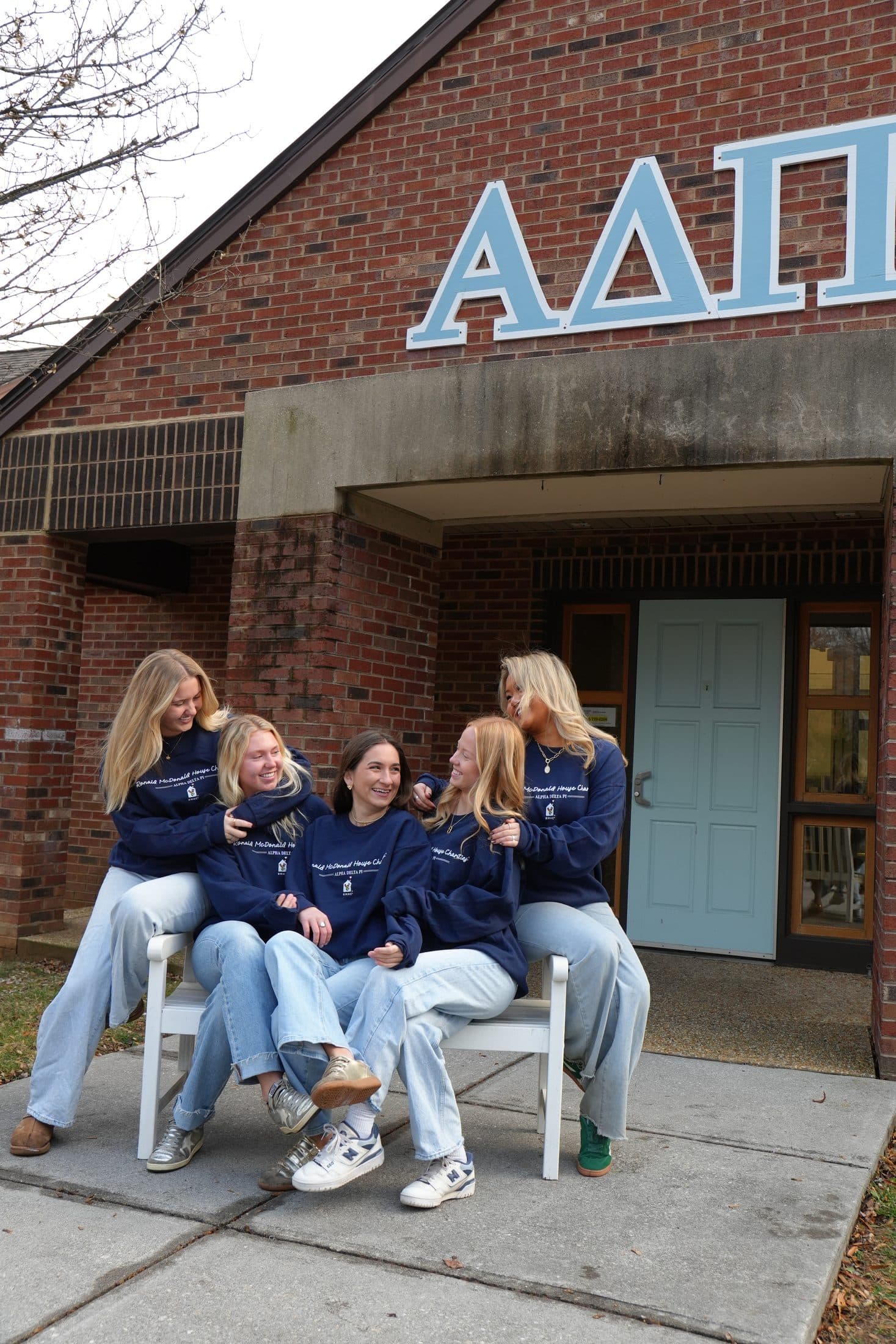 Sorority sisters in navy sweatshirts lined up along a bench