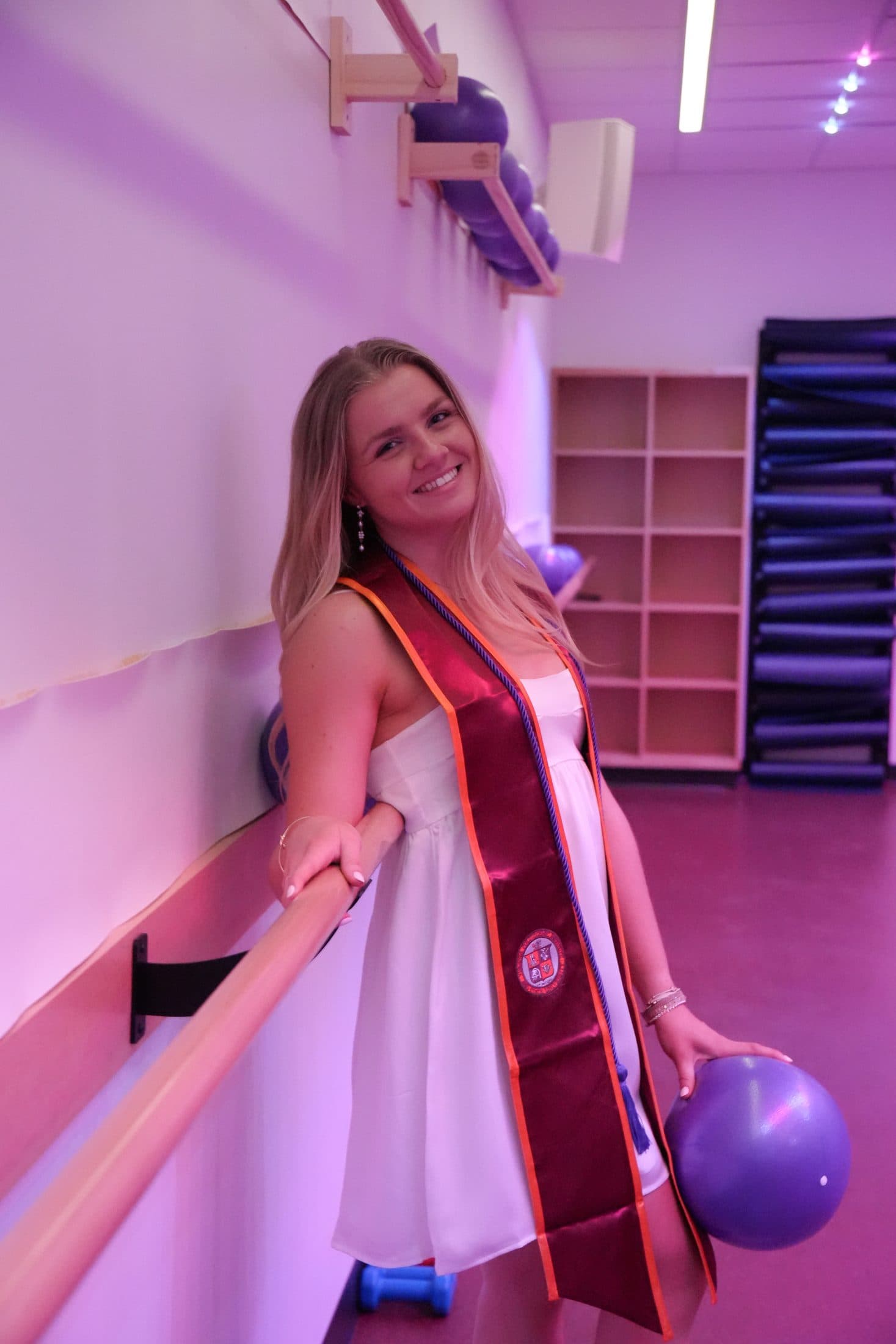 A graduate in a purple-lit corridor with a single balloon drifting nearby