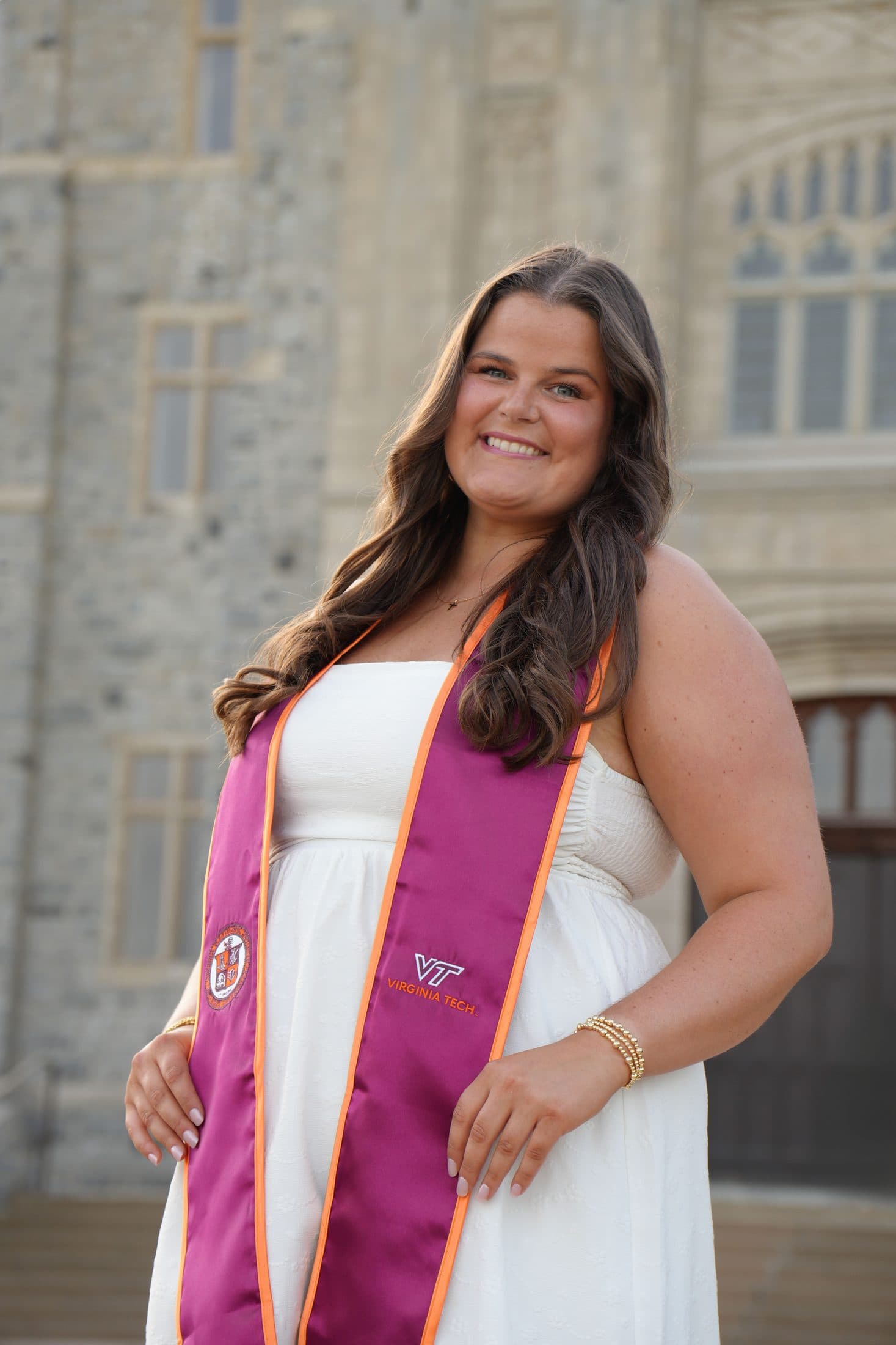A senior in a white dress and maroon stole glancing over her shoulder