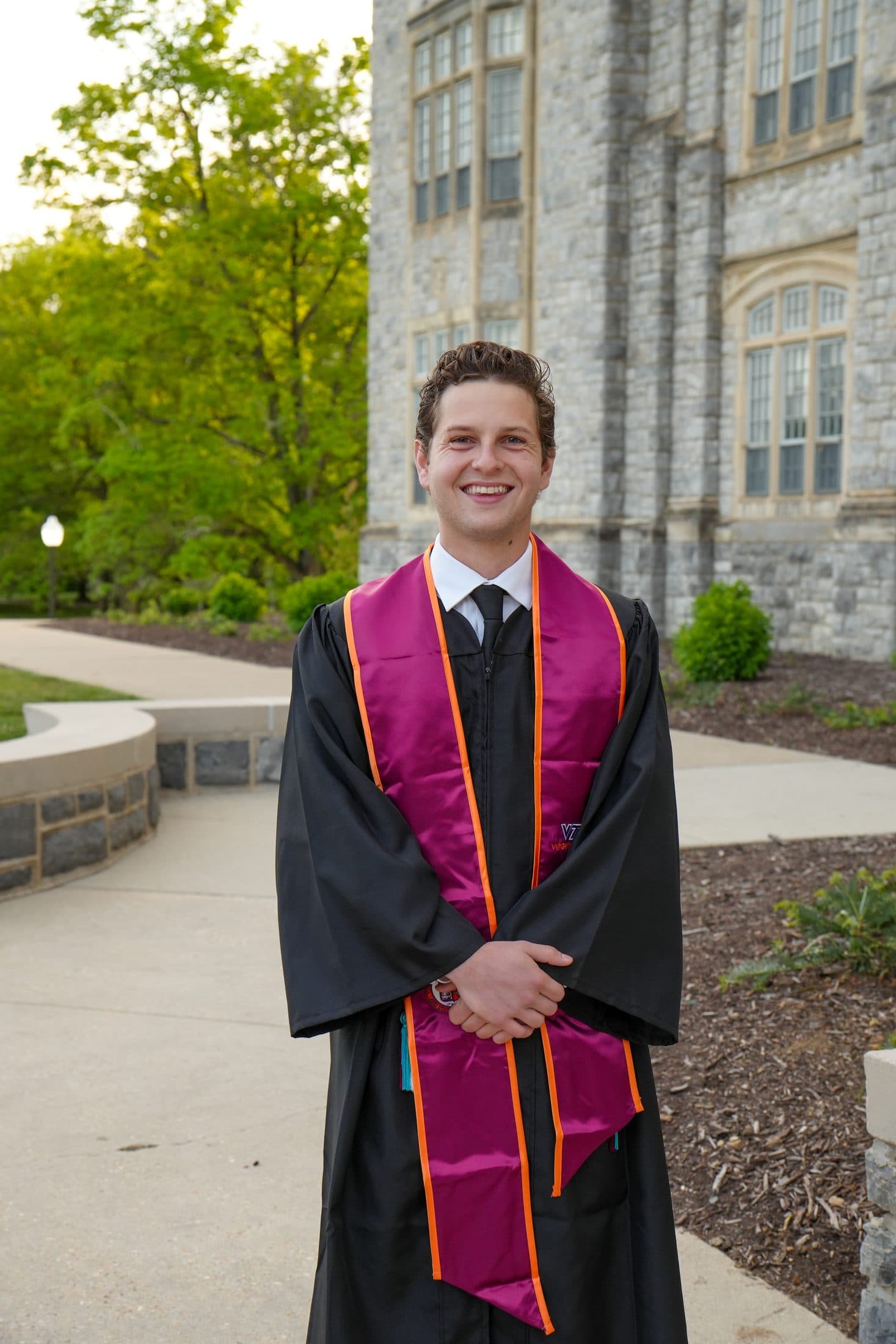 A senior in cap and gown with his maroon stole against golden foliage