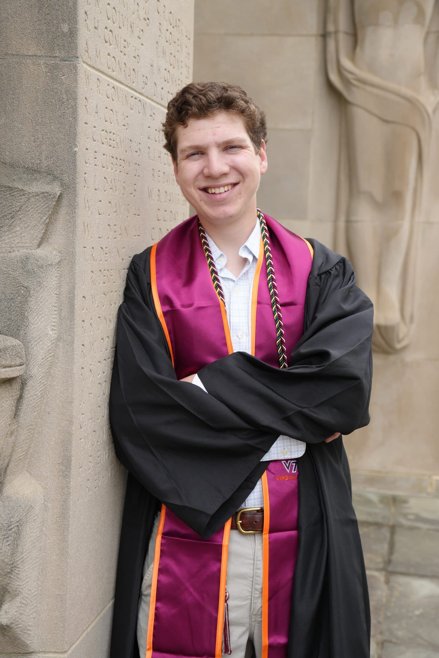 A graduate standing arms crossed and grinning in his gown
