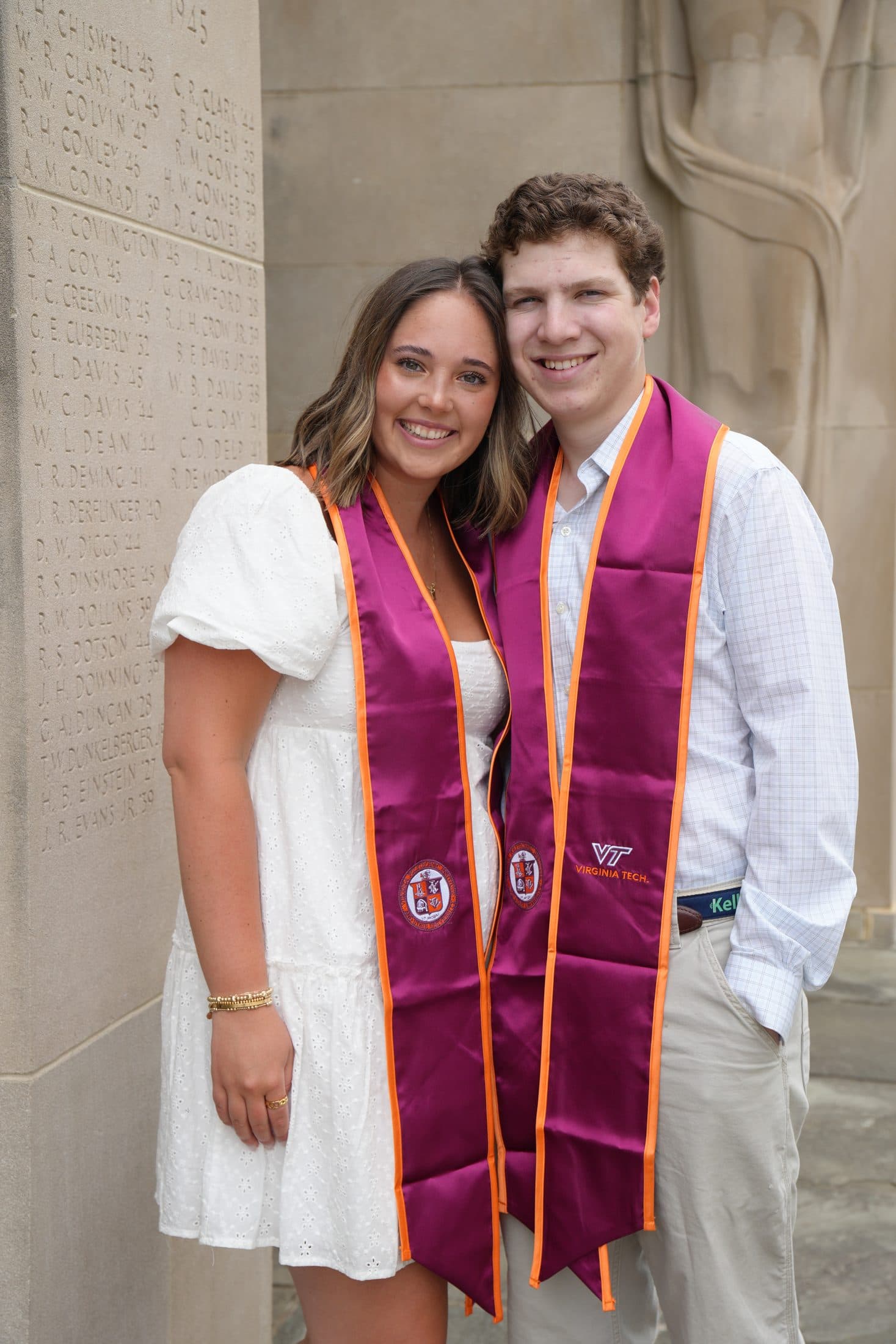 A couple in maroon stoles framed by the stone pylons of the War Memorial