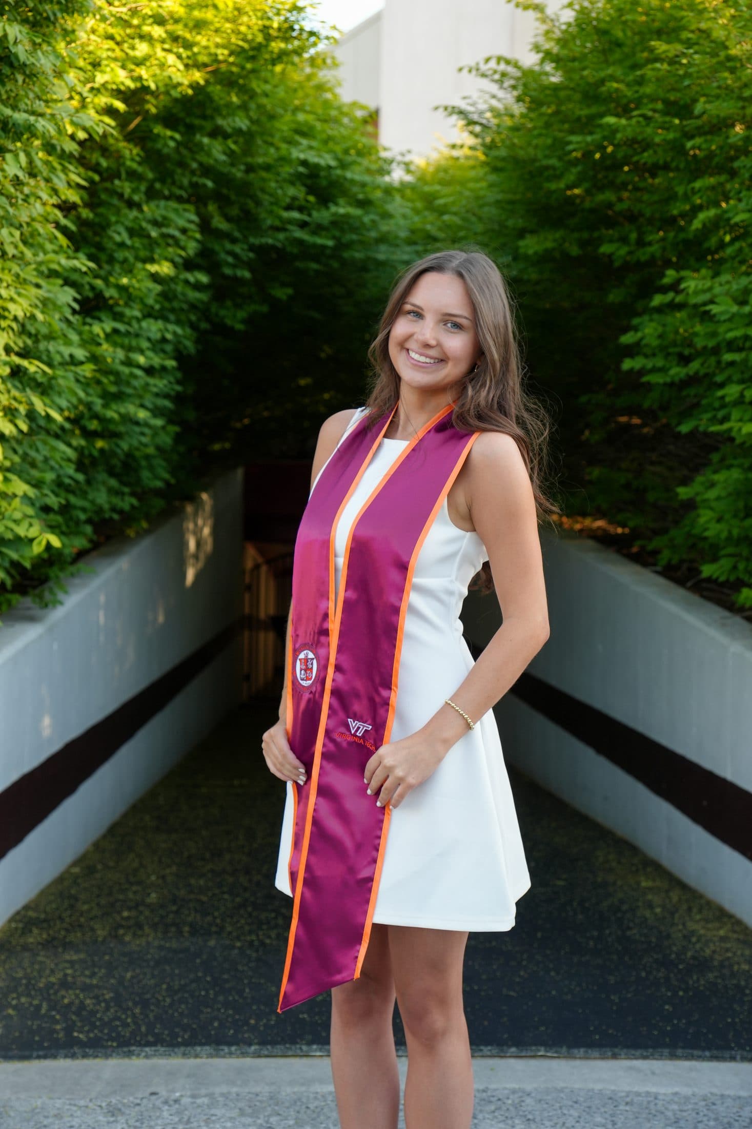 A senior walking a manicured hedge pathway in cap and gown