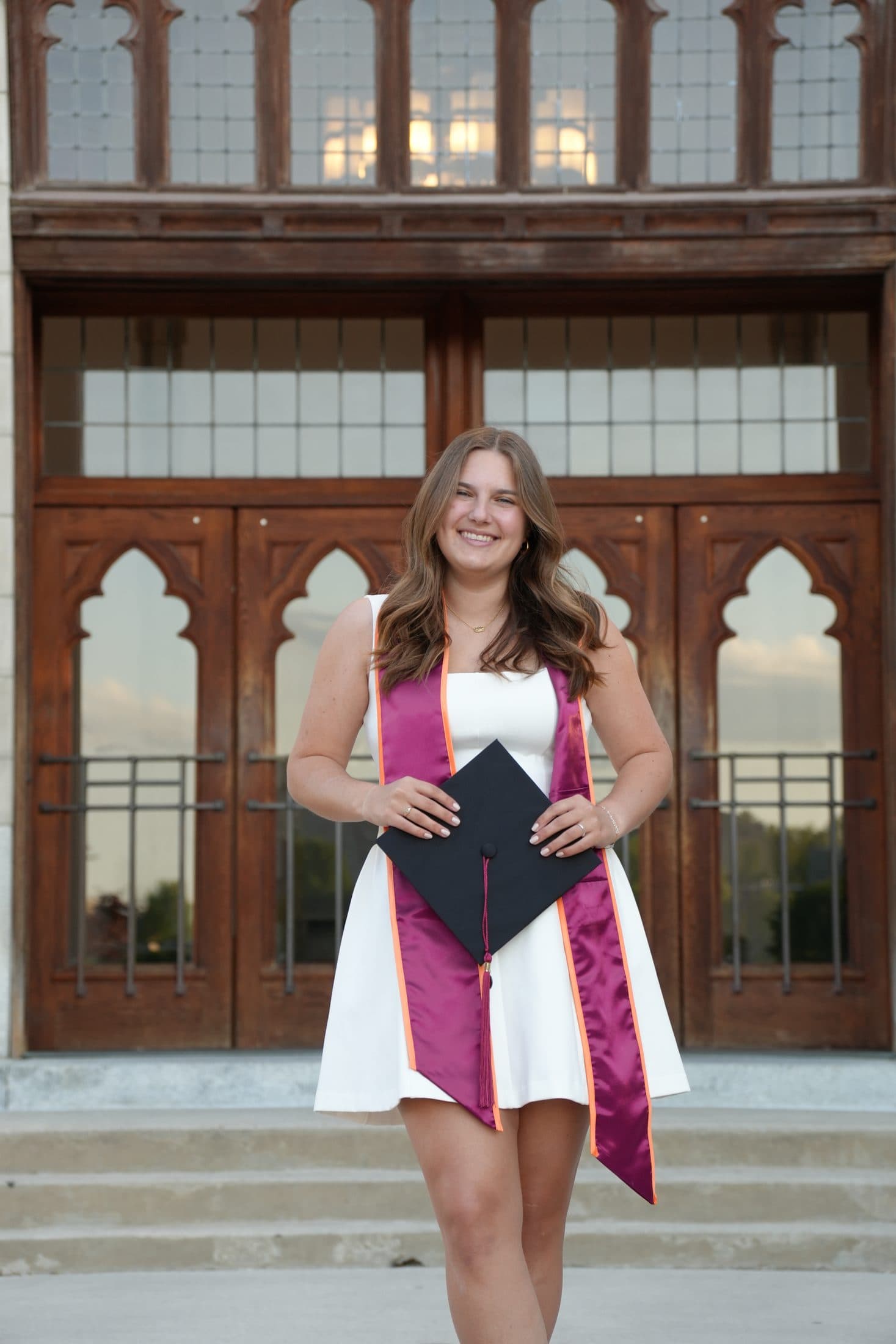 A senior holding her cap before a set of tall wooden doors
