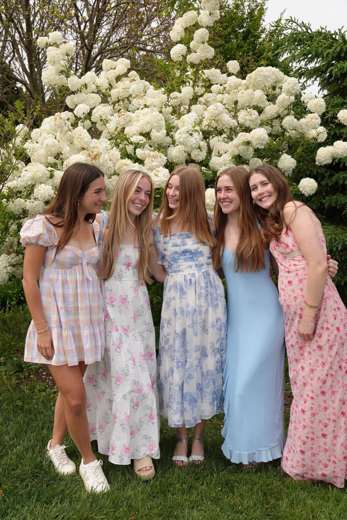 Five friends in floral dresses gathered before a wall of white hydrangeas